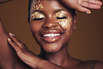 Gold, creative and art on black woman face with makeup for beauty aesthetics isolated in a studio brown background. Smile, luxury and happy person with cosmetic glamour or design for skincare