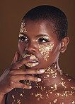 Beauty, black woman with gold paint makeup and brown background with glitter, art and cosmetics. Shine, glow and face of African model in studio for skincare, aesthetic and luxury facial with color.