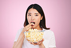 Popcorn, hungry and woman portrait eating a movie snack in a studio with watching tv and food. Pink background, Asian female person and surprise with chips in a glass bowl with film and series 