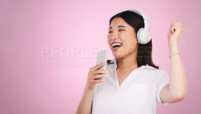 Buy stock photo Headphones, singing and woman with a phone in a studio listening to music, playlist or radio. Happy, smile and young Asian female model doing karaoke with a cellphone mic to a song by pink background