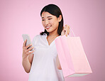 Happy asian woman, phone and shopping bag in payment, purchase or buying against a pink studio background. Female person or shopper on mobile smartphone banking app in ecommerce, sale or discount