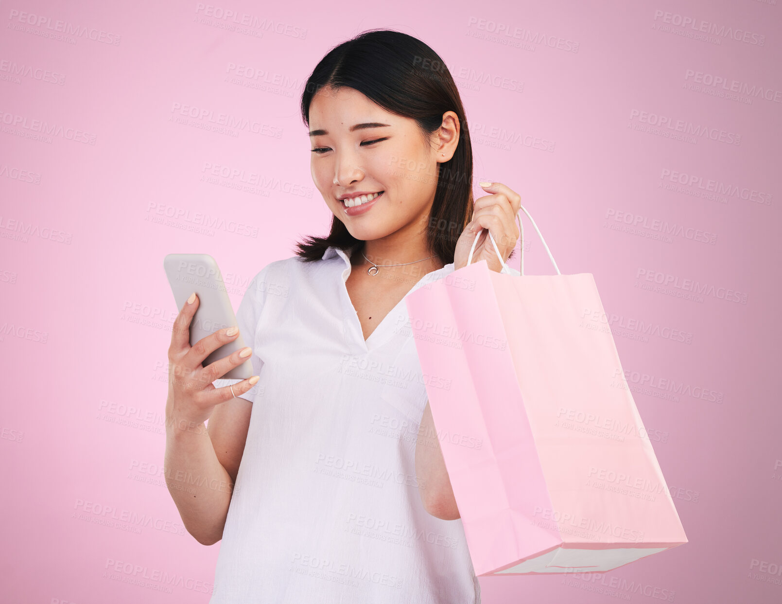 Buy stock photo Happy asian woman, phone and shopping bag in payment, purchase or buying against a pink studio background. Female person or shopper on mobile smartphone banking app in ecommerce, sale or discount