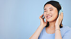 Face of happy Asian woman in studio with headphones for streaming radio, subscription and relax. Sound, smile and person listen to music, audio and track for calm on mockup space on blue background