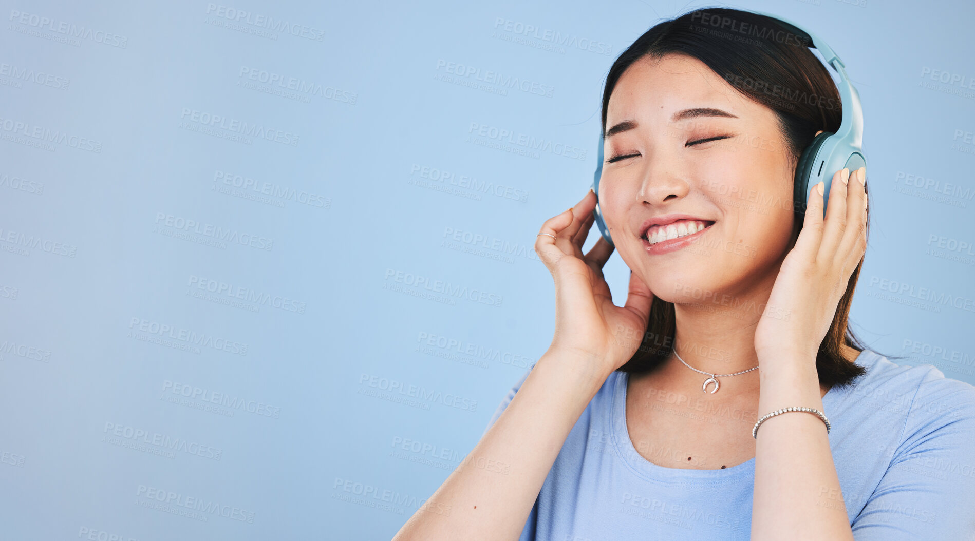 Buy stock photo Face of happy Asian woman in studio with headphones for streaming radio, subscription and relax. Sound, smile and person listen to music, audio and track for calm on mockup space on blue background
