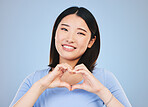 Happy asian woman, portrait and heart hands, love sign or gesture in romance against a blue studio background. Female person smile in happiness with loving emoji, shape or symbol for valentines day