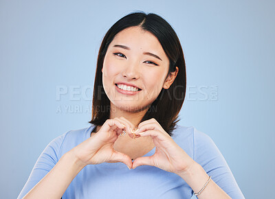 Buy stock photo Happy asian woman, portrait and heart hands, love sign or gesture in romance against a blue studio background. Female person smile in happiness with loving emoji, shape or symbol for valentines day