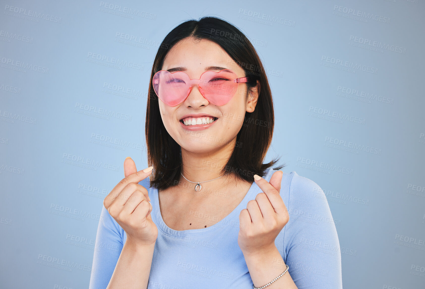 Buy stock photo Happy asian woman, portrait and sunglasses with love hands, sign or gesture against a blue studio background. Female person smile in happiness with loving emoji, icon or symbol for valentines day