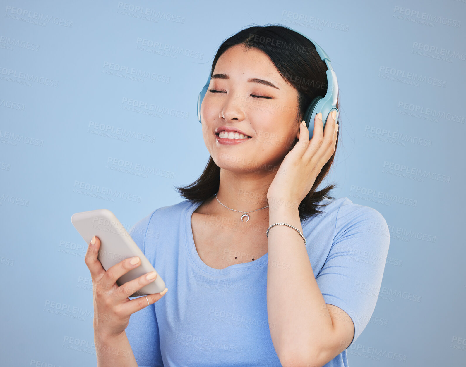 Buy stock photo Music, headphones and happy Asian woman with phone for streaming radio, subscription and relax. Sound, online podcast and face of person listening to song, audio and track for calm on blue background