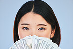 Money, beauty and woman cover face on blue background for winning, cash fan or financial prize. Lottery, portrait and asian person or winner with bonus, cosmetics secret or finance profit in studio