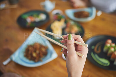 Buy stock photo Chopsticks, hand and a person eating food at a restaurant for nutrition. Closeup of a hungry woman with wooden sticks or utensil for dining, Japanese culture and cuisine on diet with sushi on menu