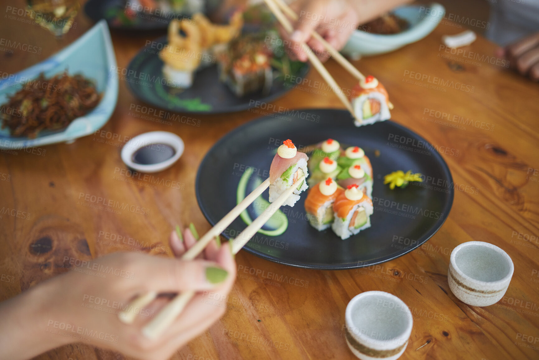 Buy stock photo Sushi, hands and eating food with chopsticks at restaurant for nutrition at table. Closeup of people with wooden sticks for dining, Japanese culture and cuisine while sharing with creativity on plate