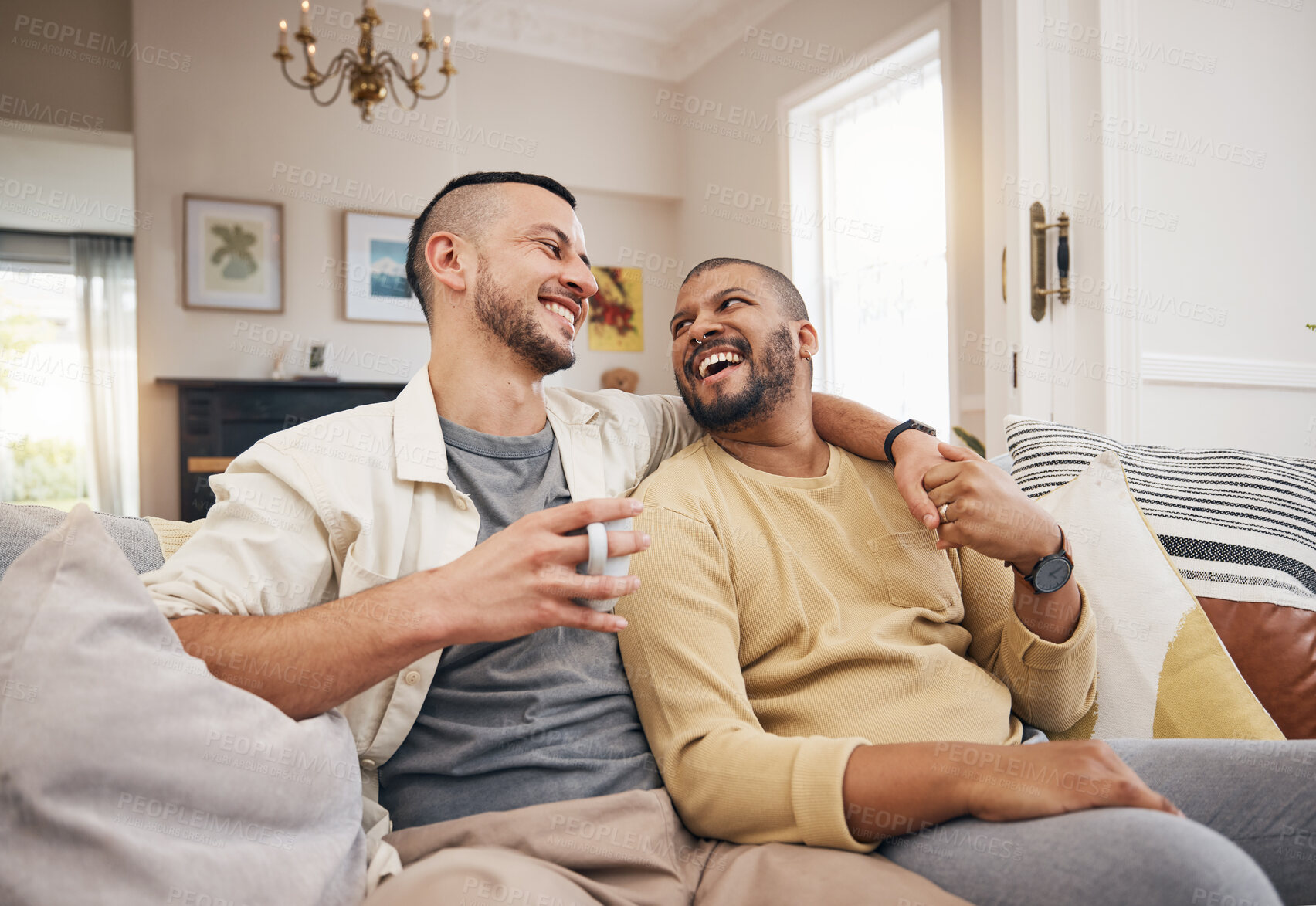 Buy stock photo Happy, home and a gay couple on the sofa with coffee, conversation or love in a house. Smile, together and lgbt men on the living room couch for a funny story, communication or speaking with tea