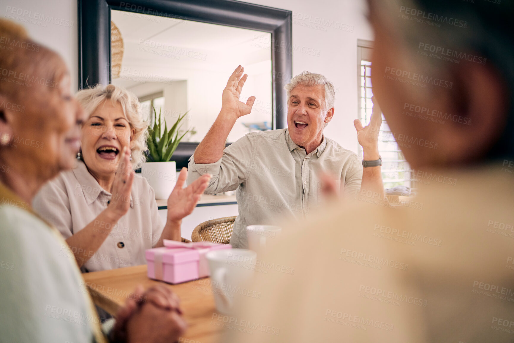 Buy stock photo Senior friends, birthday celebration and party at a home with a present and gift with excited people. Surprise, singing and retirement of elderly group at a dining room table together with a smile