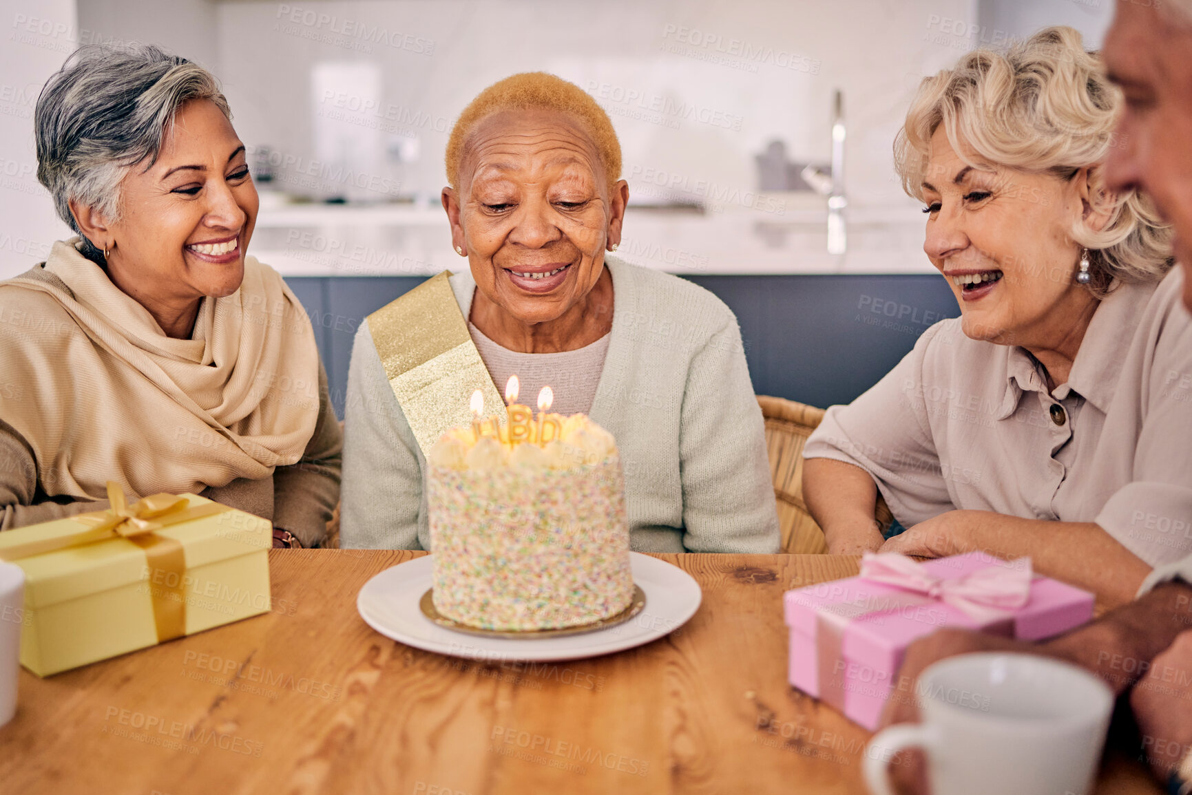 Buy stock photo Senior women, birthday cake candle and party at a home with a present and gift with excited friends. Surprise, event dessert and retirement of elderly group at dining room table together with a smile