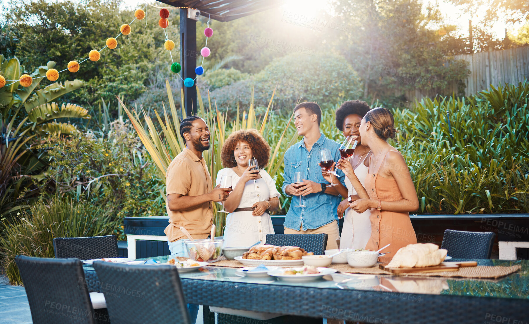 Buy stock photo Laughing, diversity and friends at lunch in a garden with drinks, conversation and talking at a party. Happy, alcohol and group of men and women at an outdoor backyard dinner with communication