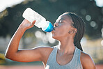 Drinking water, sports and exercise with a woman outdoor for a run, training or workout. Thirsty African athlete person at stadium for fitness and body wellness with a bottle for hydration and break