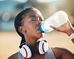 Black woman, drinking water and health, fitness and runner outdoor with headphones, thirsty after workout with cardio. Bottle, hydration and h2o, exercise and wellness with athlete, music and sports