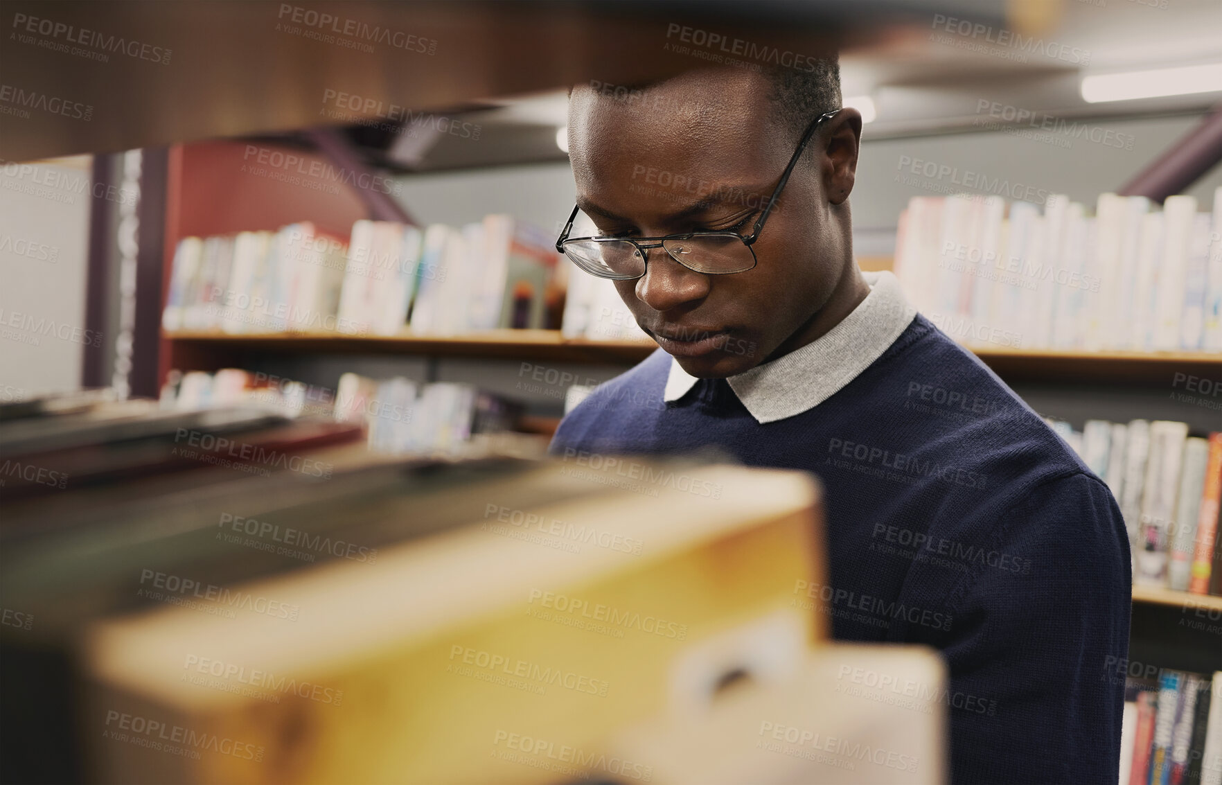 Buy stock photo University, student and black man in a library reading and learning on campus for knowledge and education in college. Smart, clever and person doing research with books on a shelf for an exam