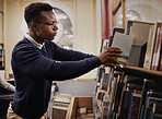 University, research and man in a library reading and learning on campus for knowledge and education in college. Smart, clever and young person in an academy with books on a shelf for an exam