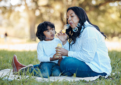 Buy stock photo Bubbles, nature and mother with child on a picnic for bonding time together on grass in summer. Happy, love and young mom with her boy baby kid blowing liquid for playing in an outdoor green garden.