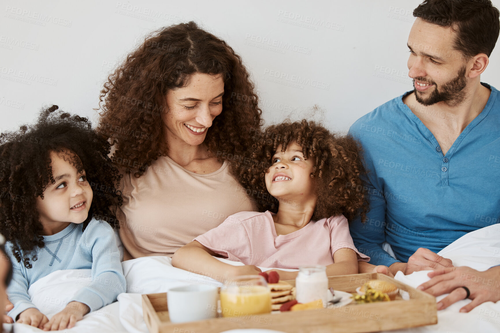 Buy stock photo Parents, children and happy family breakfast in bed, eating food and rest together, bond and relax in apartment. Home bedroom, morning meal and interracial kids, mom and dad wellness, love and care