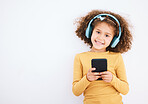 Girl child, portrait and smartphone, headphones and music with smile isolated on white background. Technology, audio streaming and social media, mockup space and kid, mobile app and radio in studio