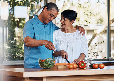 Buy stock photo Happy couple, love and hug while cooking food, cutting carrot and prepare vegetables for salad at home. Mature man, smile and embrace woman in kitchen to make healthy lunch, meal and diet for dinner