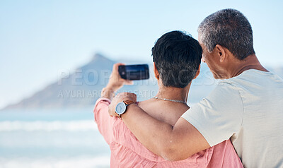 Beach, photography and back of elderly couple hug in nature for travel, freedom and photo memory. Smartphone, profile picture and rear view of seniors at sea for retirement trip, selfie or vacation