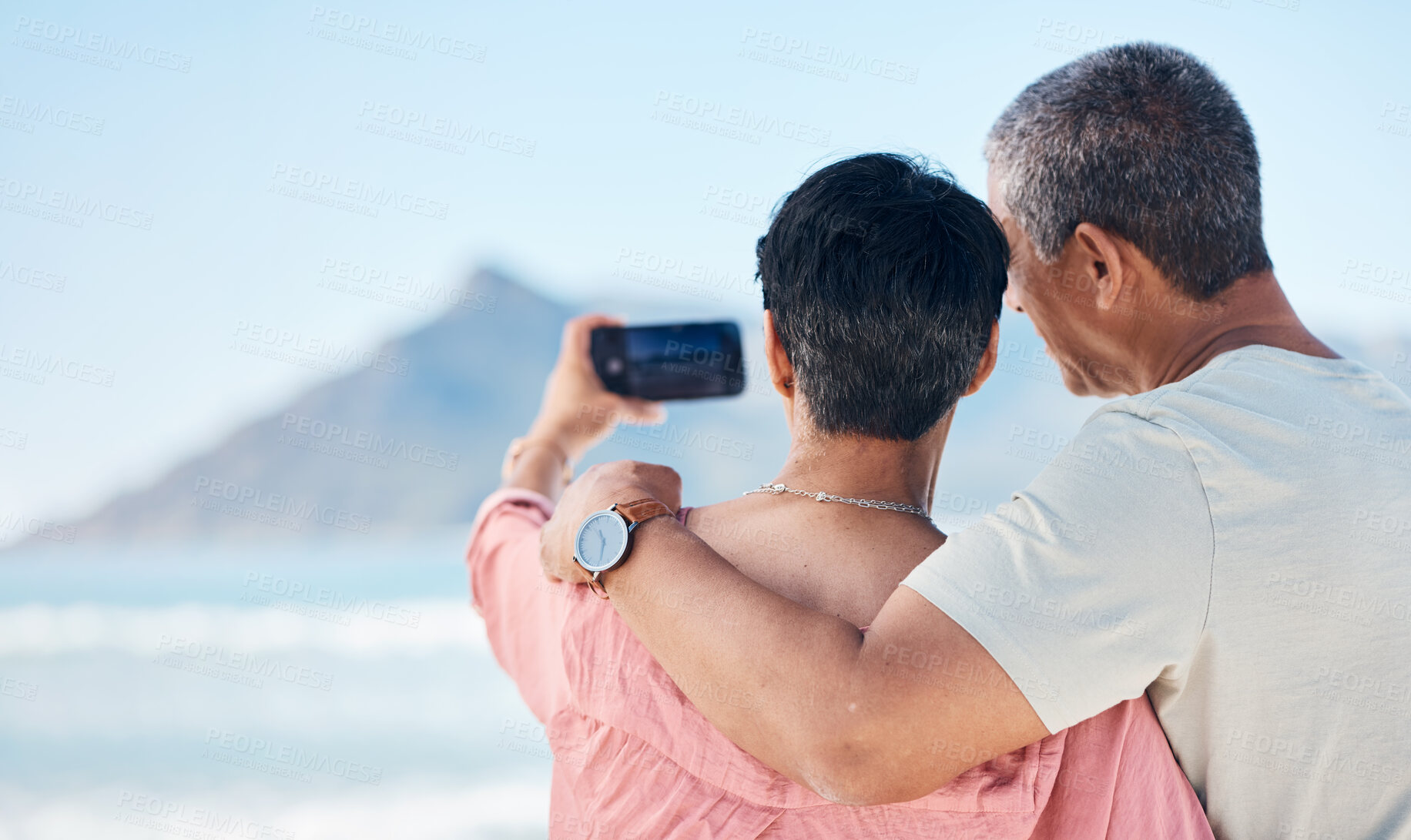 Buy stock photo Beach, photography and back of elderly couple hug in nature for travel, freedom and photo memory. Smartphone, profile picture and rear view of seniors at sea for retirement trip, selfie or vacation