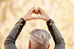 Nature, heart shape and back of man in a park for race, marathon or competition run training. Fitness, sports and closeup of an elderly male athlete with a love hand gesture in an outdoor garden.