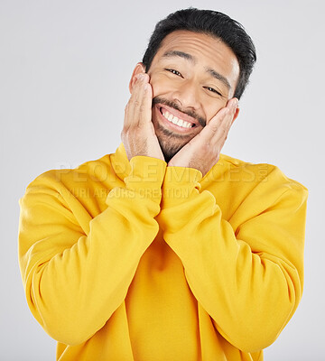Buy stock photo Smile, shy and hands on face of asian man in studio for in love, sweet or gesture on grey background. Happy, portrait and Japanese male model pose with emoji cheeks expression for romantic sign

