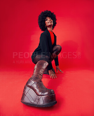 Buy stock photo Fashion, boots and portrait of a black woman on a red background in studio to model trendy footwear. Style, clothes and smile with a happy young afro female posing for advertising or marketing