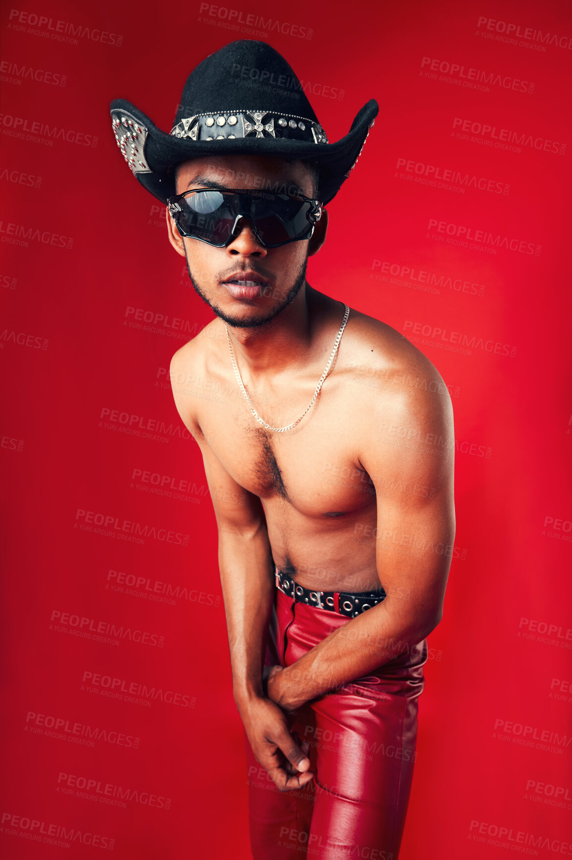 Buy stock photo Fashion, man and cowboy hat, sunglasses and shirtless, clothes and gen z isolated on red background. Confident model, cool and leather pants with eyewear accessory, western aesthetic in a studio