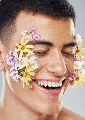 Buy stock photo Smile, beauty and a man with flowers on a studio background for creative aesthetic. Happy, plant and a male model with floral art for facial wellness and dermatology isolated on a studio backdrop