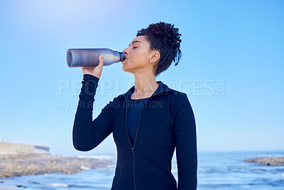Buy stock photo Fitness, woman and drinking water at beach for running, health or morning cardio on blue sky by an ocean. Exercise, hydration and thirsty lady runner with sports liquid after training or sea workout