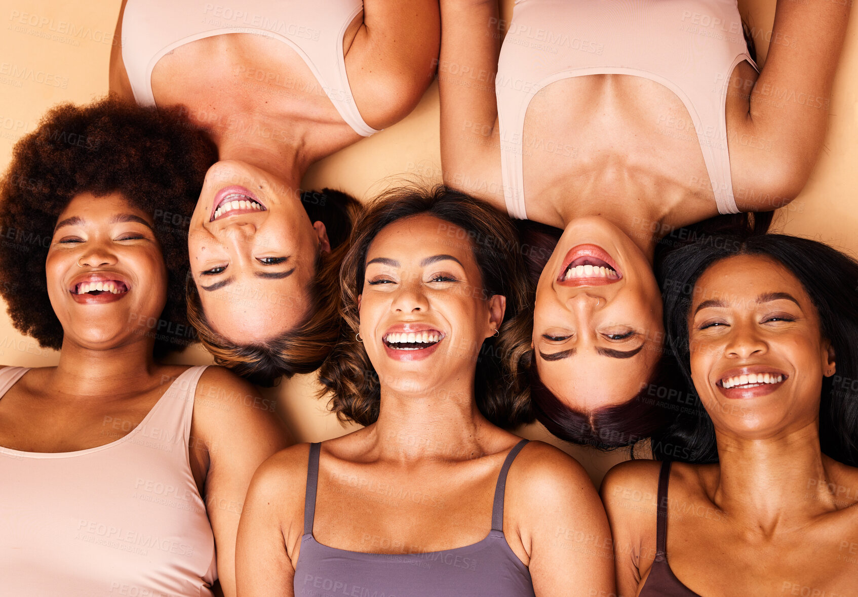 Buy stock photo Diversity, beauty and portrait of women from above with smile, self love and solidarity in studio. Happy face, group of friends on beige background with underwear, skincare and cosmetics on floor.