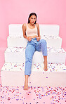Woman, confetti and sitting on steps portrait with relax, style and fashion with celebration sparkle. Studio, pink background and model with party, event and birthday decoration with confidence