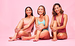 Beauty, bikini and group of women in studio, sitting together with smile and body positivity portrait. Diversity, summer fashion and happy swimwear models with self love, equality and pink background