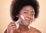 Black woman, face roller and portrait of beauty, rose quartz cosmetics and natural skincare on studio background. Happy model, facial massage and crystal tools for dermatology of lymphatic drainage