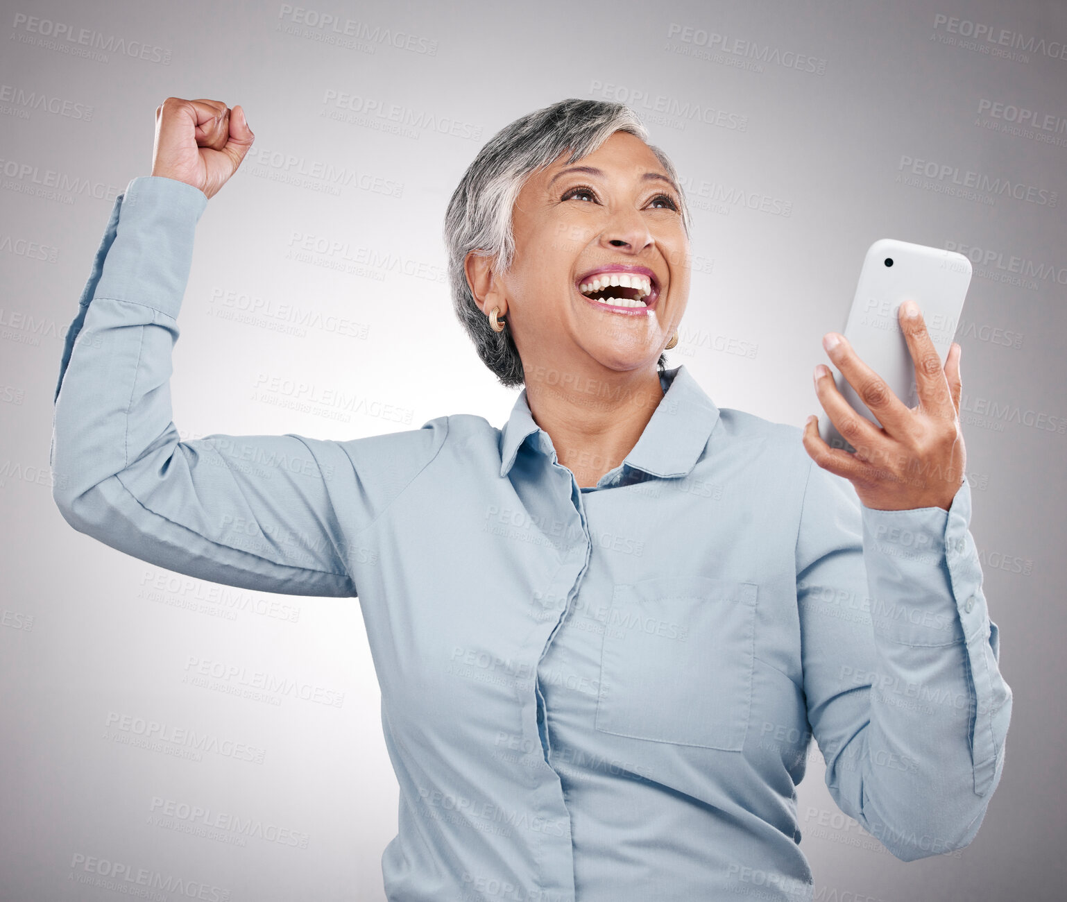 Buy stock photo Winner, cellphone and senior woman in studio winning an online bet, good news or prize. Happy, celebration and elderly female model with fist pump for success on a phone isolated by gray background.