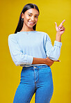 Pointing, mockup and portrait of a woman in a studio for advertising, marketing or promotion. Smile, happy and young Indian female model with a direction hand gesture isolated by yellow background.