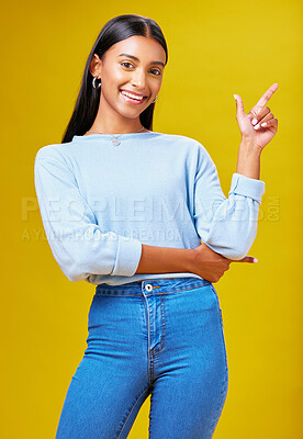 Buy stock photo Pointing, mockup and portrait of a woman in a studio for advertising, marketing or promotion. Smile, happy and young Indian female model with a direction hand gesture isolated by yellow background.