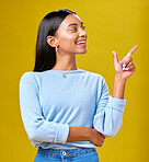 Pointing, smile and young woman in a studio for advertising, marketing or promotion. Happy, excited and Indian female model with a direction or arrow hand gesture isolated by yellow background.