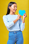 Donation, smile and woman with blue heart in studio for help, hope or empathy on yellow background. Charity, lady or social media poster for thank you, support for autism or people with a disability