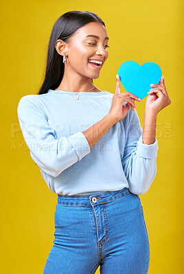 Buy stock photo Donation, smile and woman with blue heart in studio for help, hope or empathy on yellow background. Charity, lady or social media poster for thank you, support for autism or people with a disability
