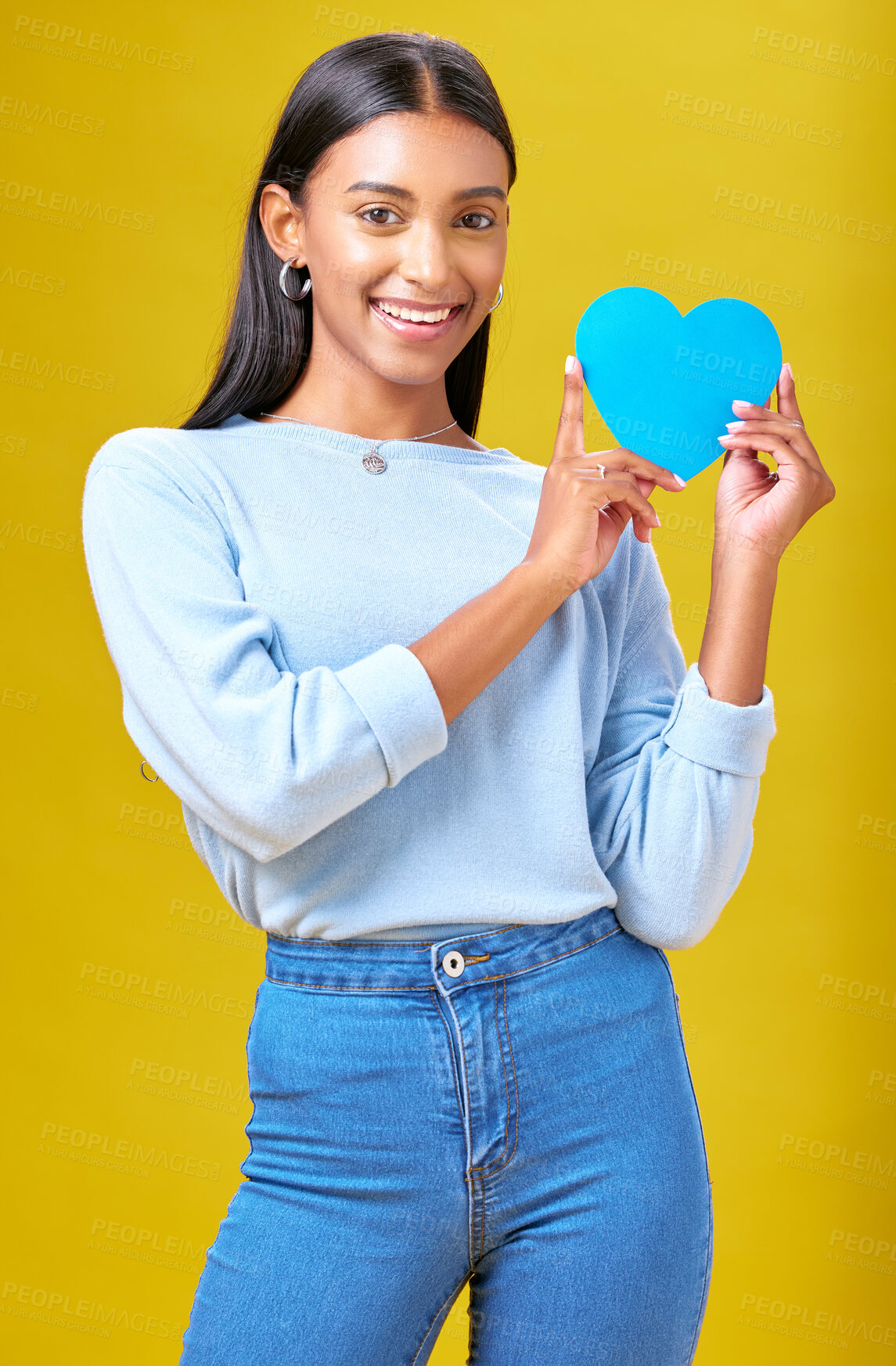 Buy stock photo Portrait, smile and woman with blue heart in studio with help, hope or empathy on yellow background. Face, girl and social media icon for thank you, support and trust or people with loyalty to peace