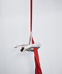 Gymnastics, acrobat and aerial silk with a woman in air for performance, sports and balance. Young athlete person or gymnast hanging on red fabric and white background with space, art and creativity