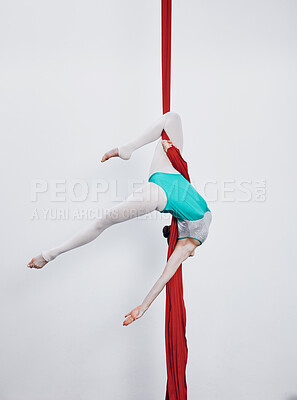 Aerial silk, acrobat and gymnastics with a woman in air for performance, sports and balance. Young athlete person or gymnast hanging on red fabric and white background with space, art and creativity