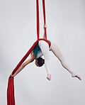 Silk, gymnastics and aerial acrobat or woman in air for performance, sports and balance. Flexible athlete person or gymnast hanging on red fabric and white background with space, art and creativity