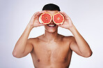 Beauty, grapefruit and skincare with face of man in studio for health, detox and natural cosmetics. Vitamin c, nutrition and summer with person and fruit on white background for self care and glow 